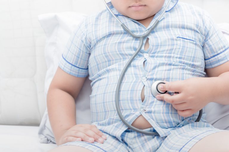 Overweight child wearing a tight button down shirt with a stethoscope on his stomach