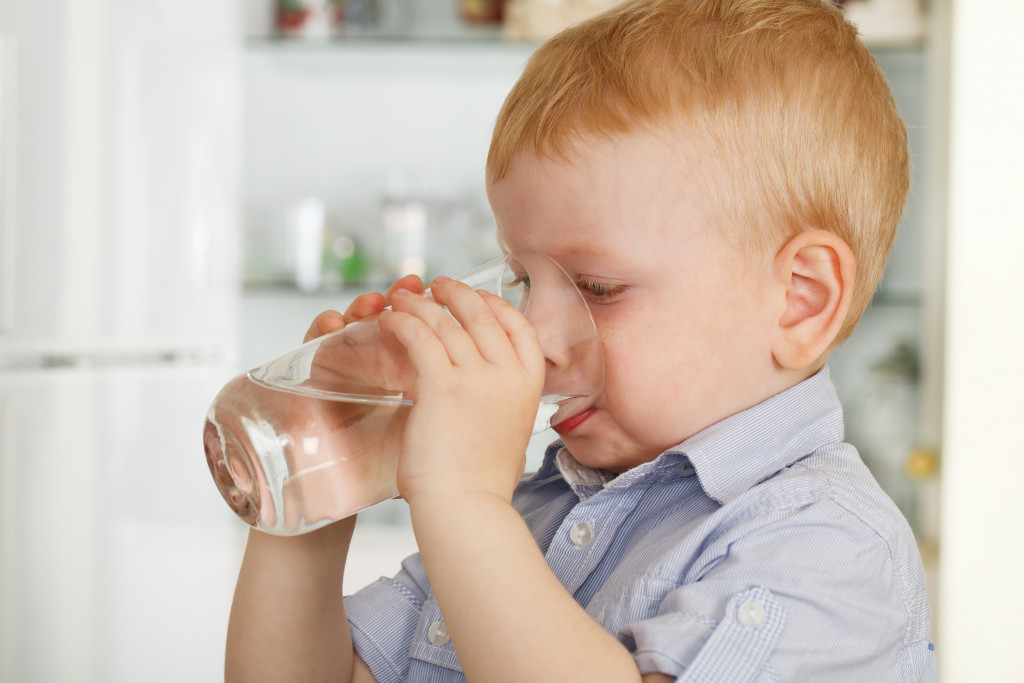 A young boy drinking a glass of water in the kitchen