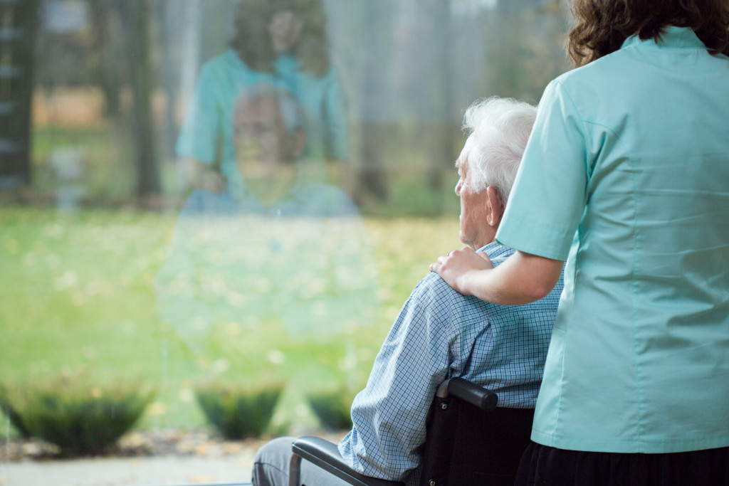 A caregiver and an elderly man on a wheelchair looking out the window