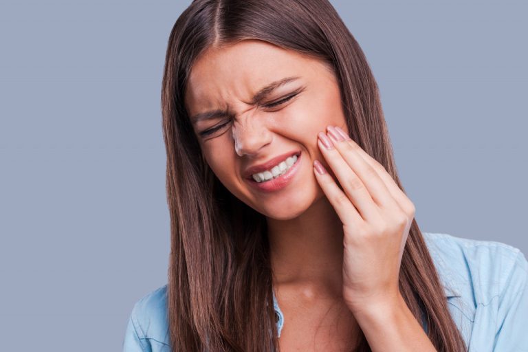 young woman suffering from toothache against gray background