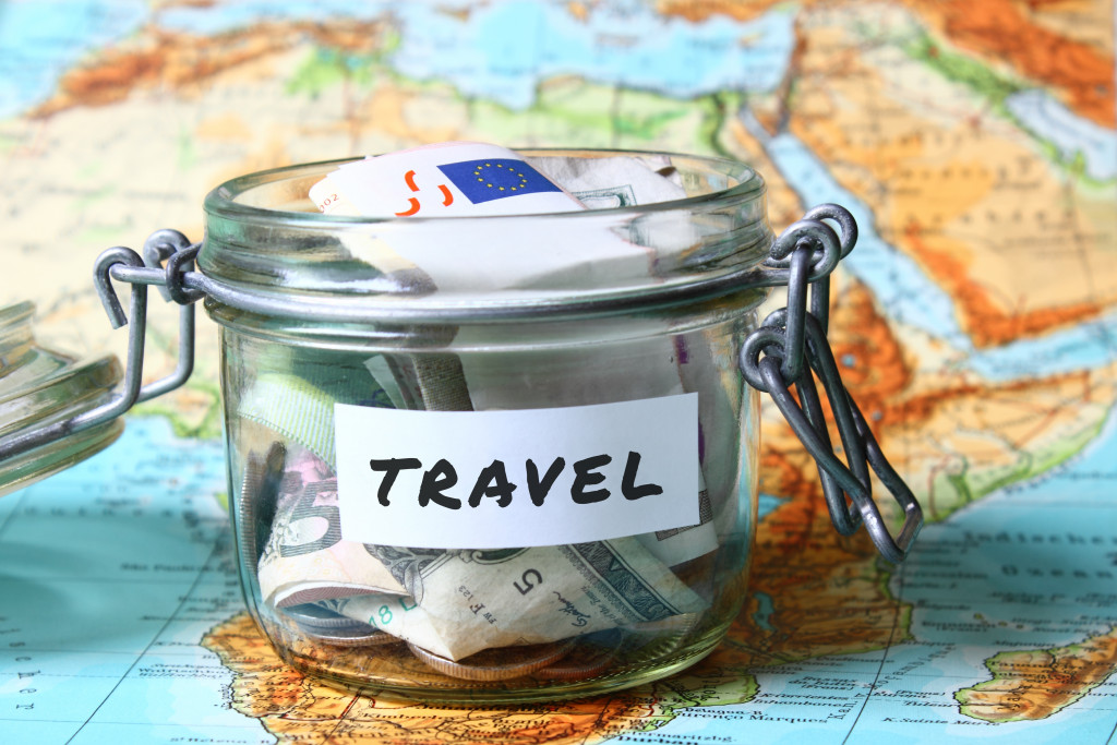 Money in a glass jar labeled travel on a world map