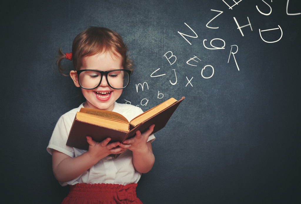 little girl reading with glasses with letters flying out