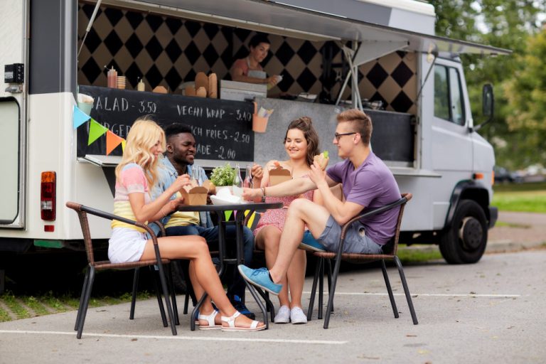 Group of friends eating and talking on a table beside a food truck